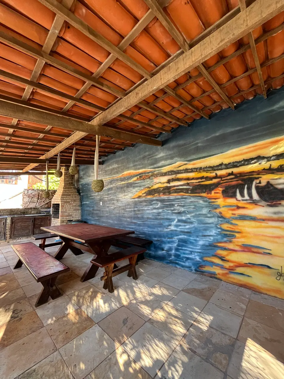 Área de churrasqueira com mural pintado do pôr do sol na praia
