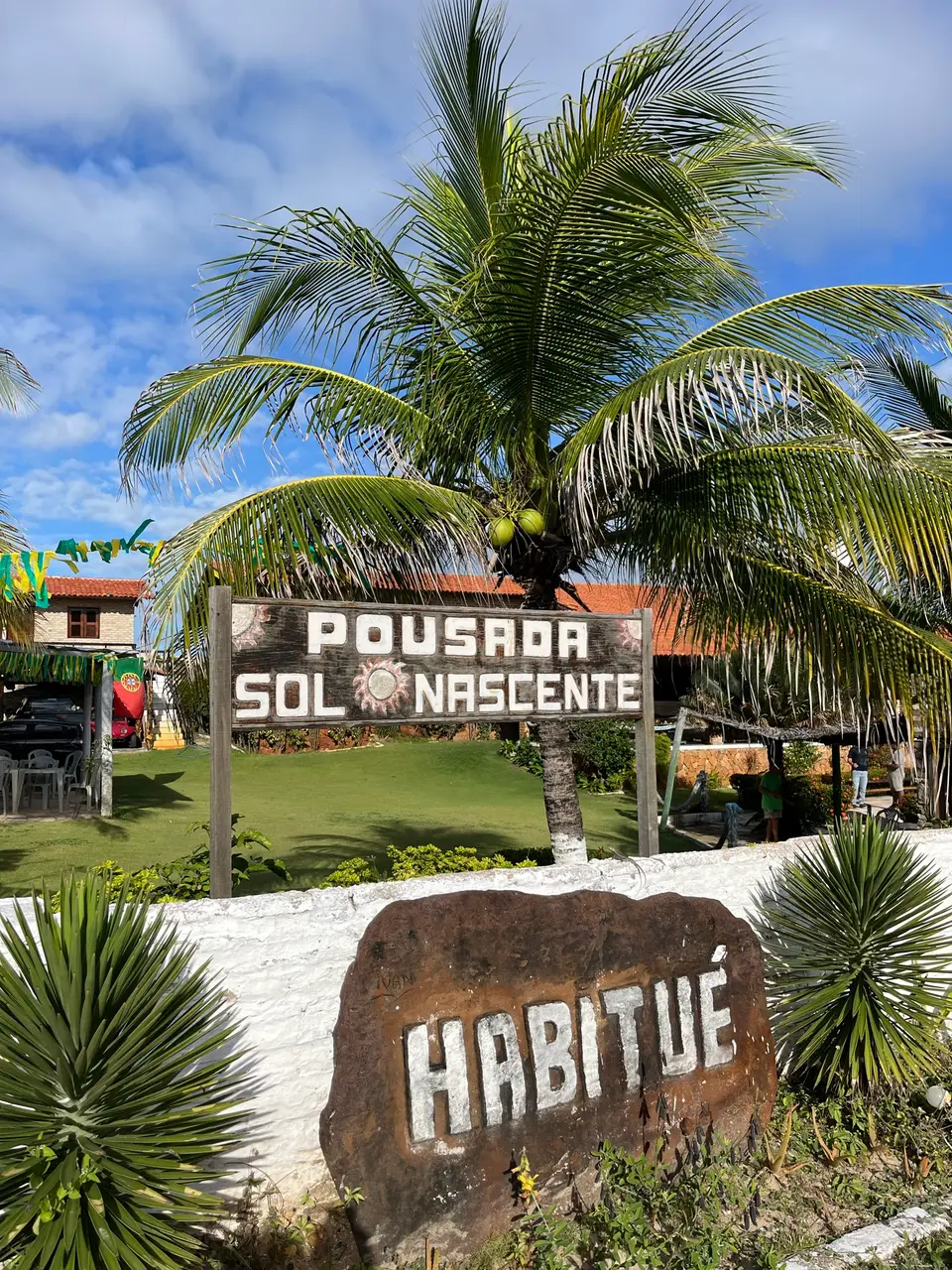 Placa de madeira da Pousada Sol Nascente entre coqueiros