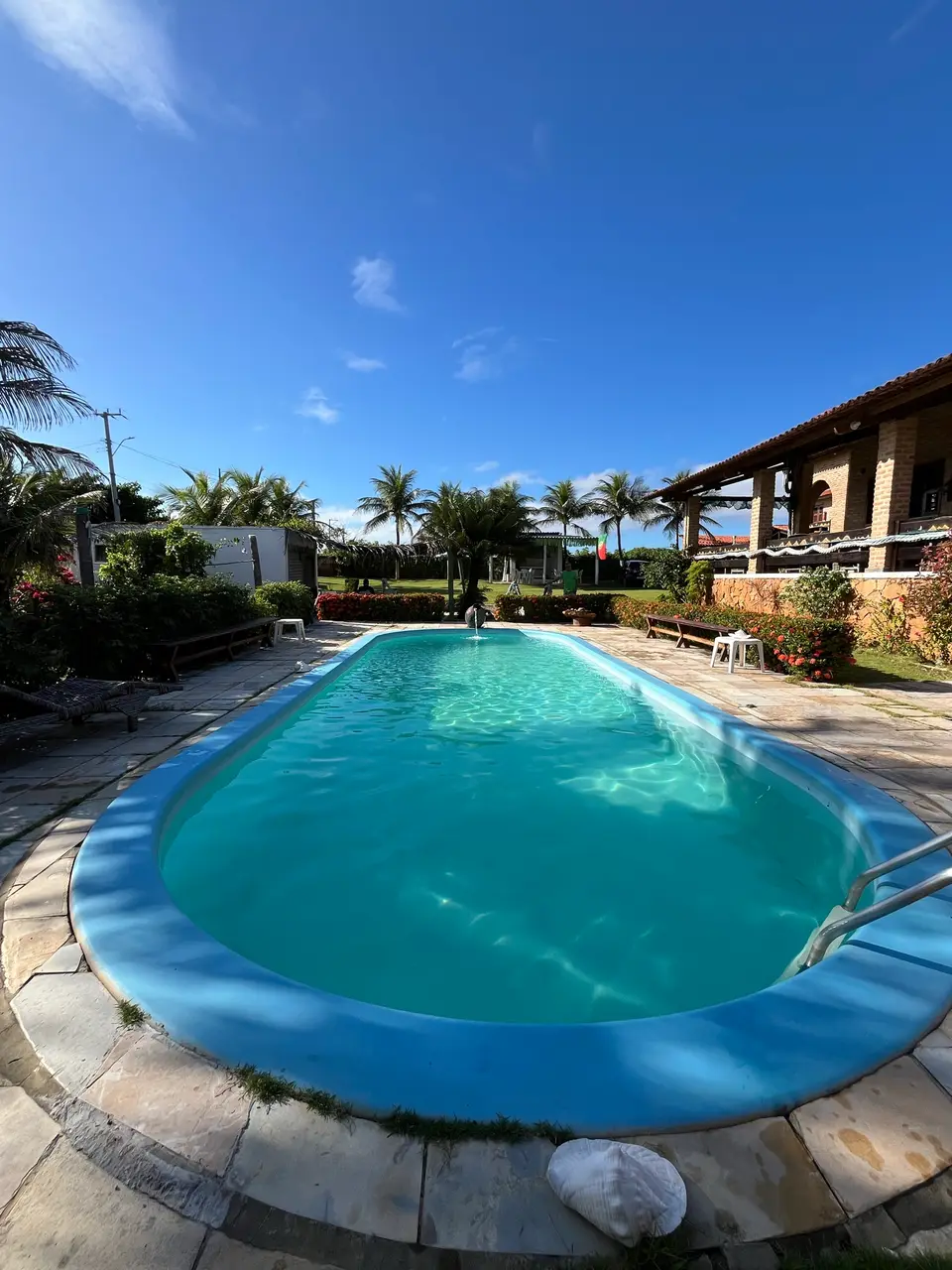 Piscina oval com coqueiros e a varanda da pousada ao fundo